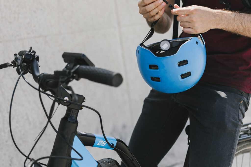 Person holding a blue bicycle helmet while standing next to a blue e-bike, adjusting the helmet straps.