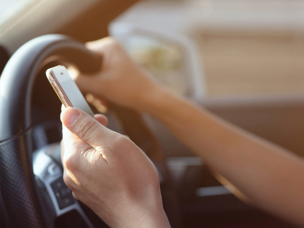 A driver holding a cellphone while behind the wheel, illustrating a violation of Colorado’s hands-free law.