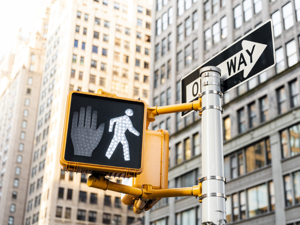 A close-up of a pedestrian crossing signal and a one-way sign in a city, representing legal challenges and Colorado pedestrian deaths.