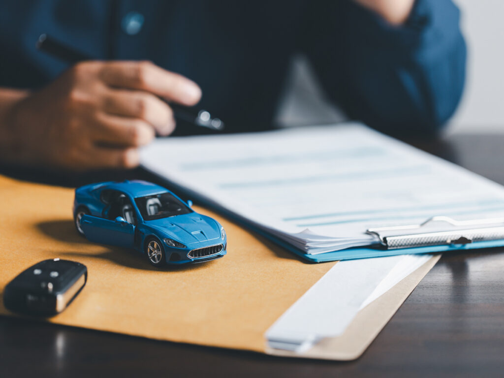 Person reviewing car insurance policy documents with a toy car and keys in the foreground.