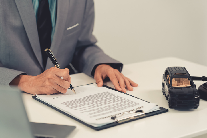 A representative for automotive litigation, auctions, and claims is depicted with a gavel and a miniature model car on a wooden table, creating a concept related to car auctions.